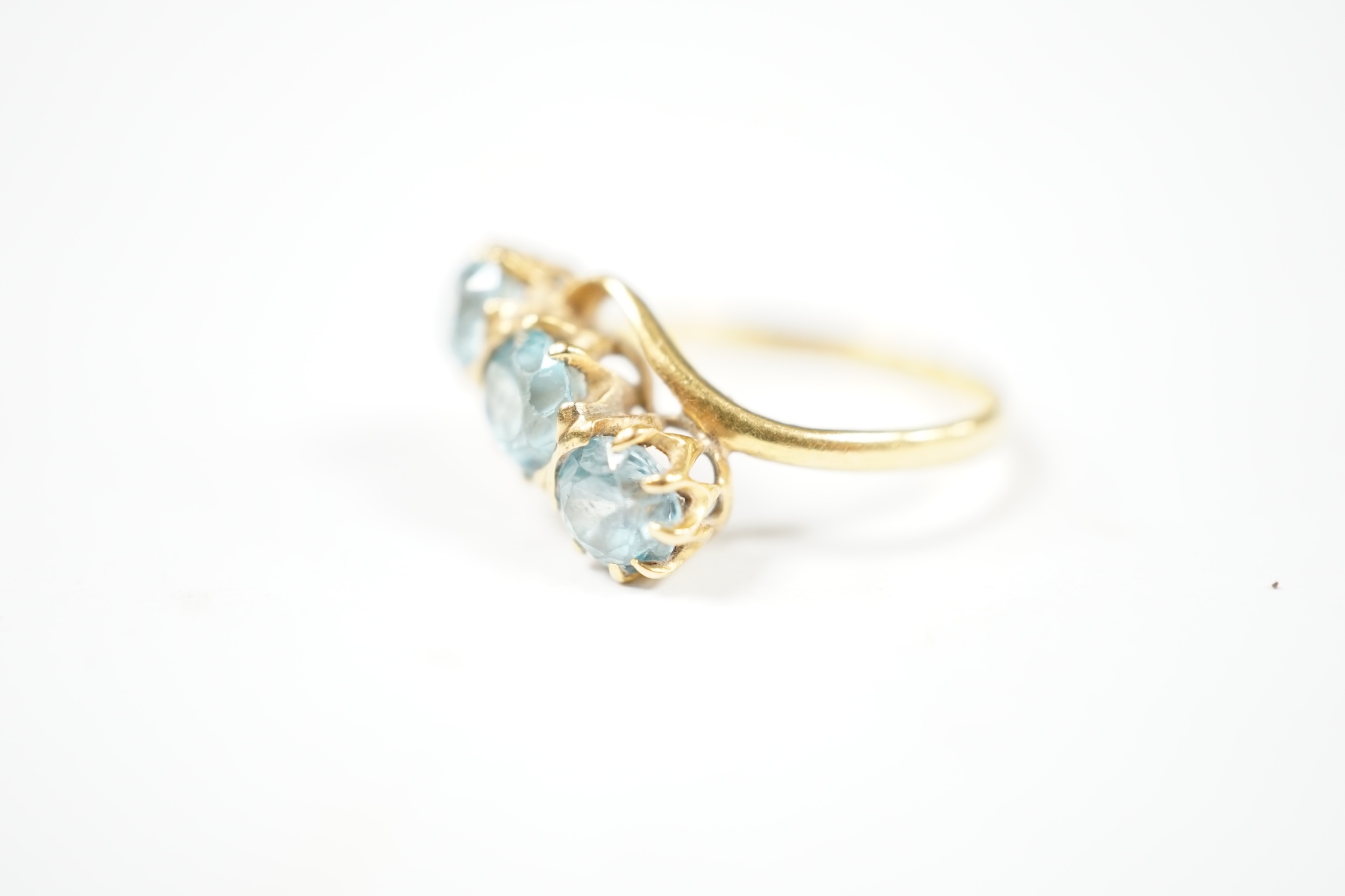 A yellow metal and three stone blue zircon set crossover ring, size L, gross weight 3 grams. Condition - poor